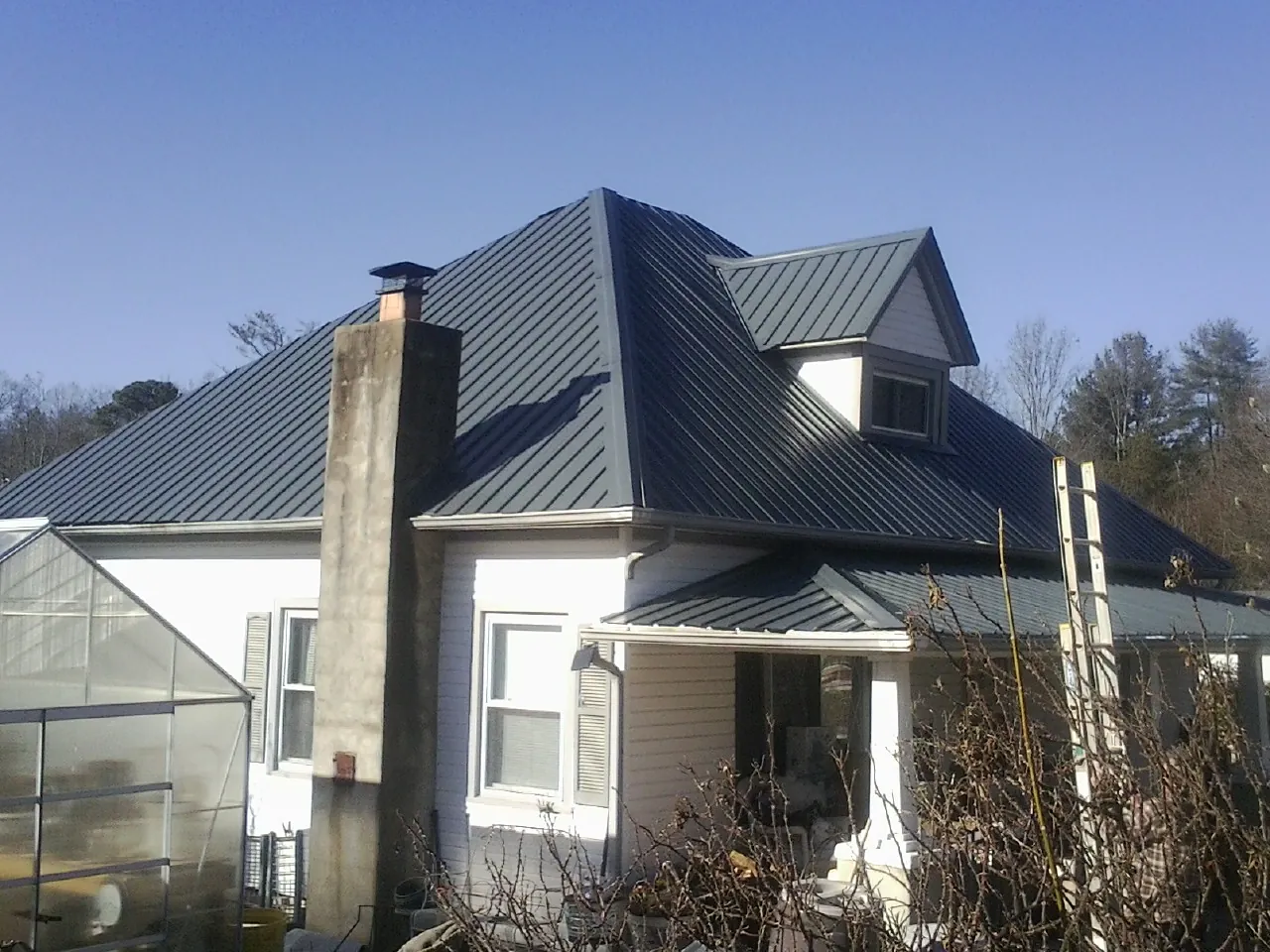 Dark blue standing seam metal roof on a white farmhouse with dormer in Leonard