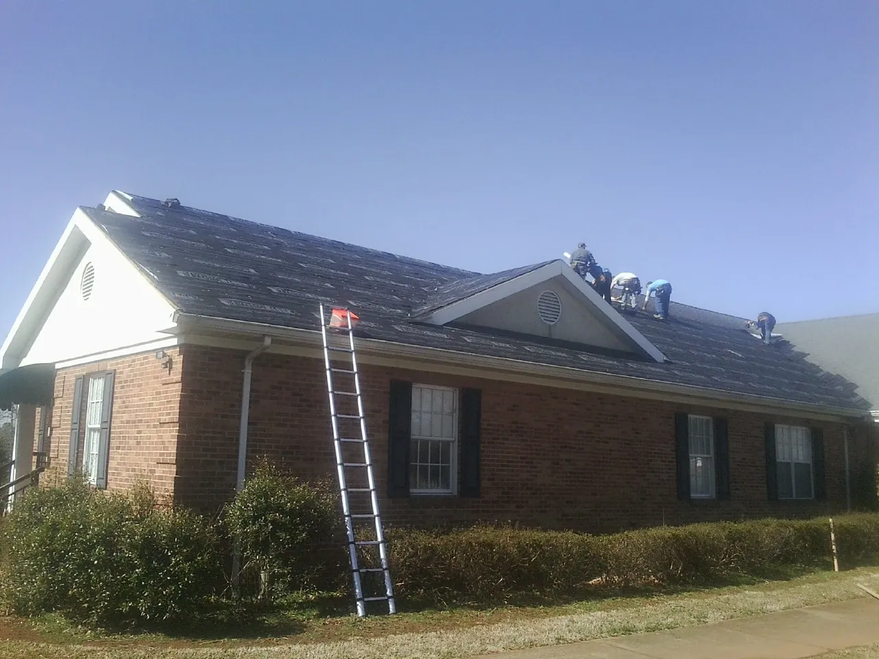 Crew tearing shingles off a brick ranch roof with a ladder set — Emergency Roof Repair work by our crew in Leonard